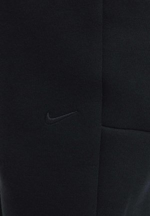 Schwarze Nike-Sweatpants mit geripptem Muster, enger Passform und einem auffälligen eingestickten Logo auf der linken Seite.