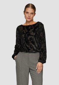Zwarte blouse met lange mouwen, zacht en fluweelachtig van textuur en een abstract patroon, gecombineerd met lichtgrijze, op maat gemaakte broek. Ronde halslijn, losse pasvorm.