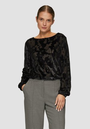 Zwarte blouse met lange mouwen, zacht en fluweelachtig van textuur en een abstract patroon, gecombineerd met lichtgrijze, op maat gemaakte broek. Ronde halslijn, losse pasvorm.