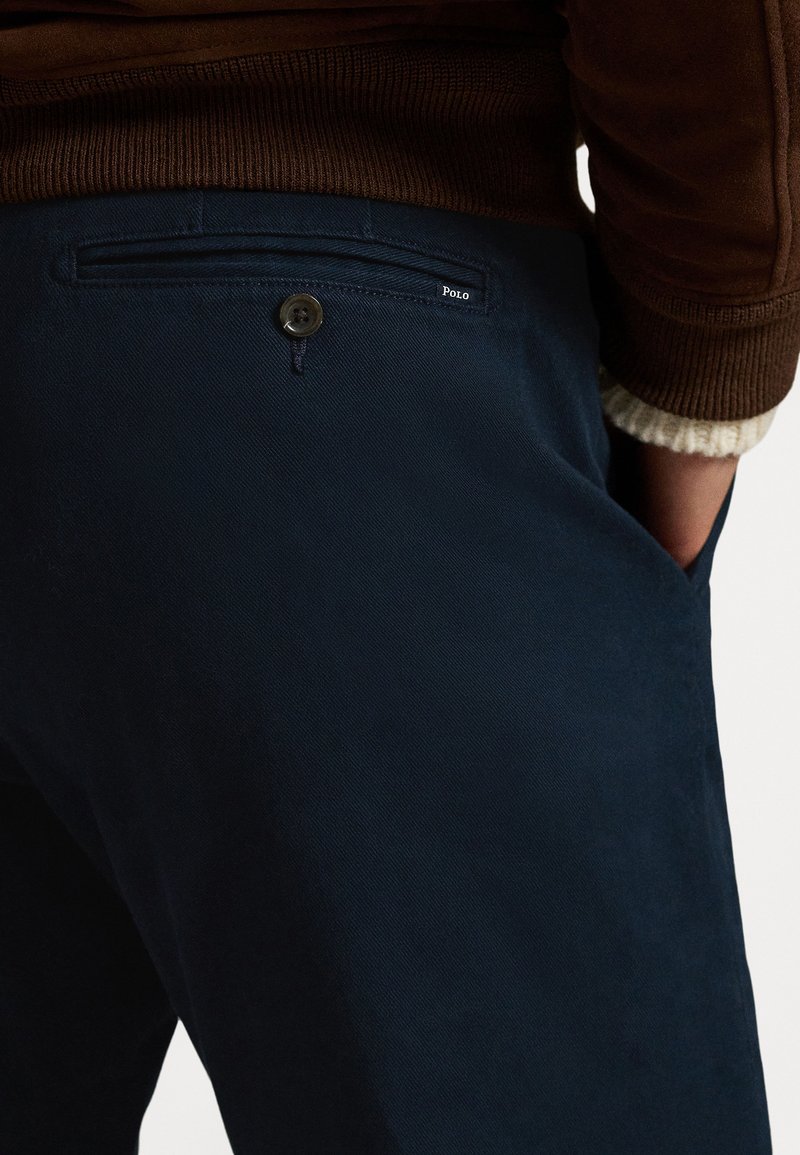 Pantaloni blu navy in tessuto morbido con chiusura a bottone e tasca posteriore. Presentano un discreto marchio "Polo" vicino alla tasca.