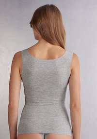 Grå ärmlös topp med en slät yta, rund halsringning och figurnära design. Bakifrån visas en konturerad form och minimala sömmar.