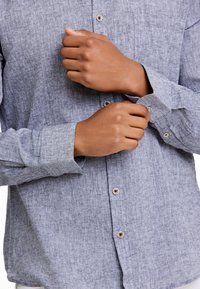 Blauw gemêleerd shirt met een button-down kraag, voorzien van knoopsluitingen en opgerolde mouwen, met een subtiel geweven patroon.
