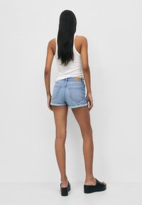 Pantalones cortos de mezclilla en azul claro con dobladillo deshilachado y puños enrollados, combinados con una camiseta sin mangas blanca y sandalias de plataforma negras.