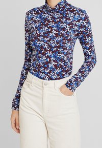 Langærmet turtleneck top med et blomsterdesign i blå og hvid på en mørk maroon baggrund, lavet af strækbart stof.