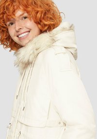 Biała parka z miękkim sztucznym futrem przy kapture, z suwakiem i zapięciem na guziki, bocznymi kieszeniami oraz regulowanym wiązaniem w talii.