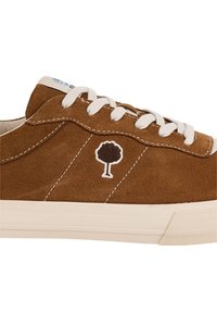 Sneaker in suede marrone con lacci bianchi, cuciture bianche, un piccolo logo ad albero sul lato e una suola in gomma beige su sfondo bianco.