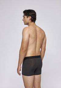 Schwarze Stoff-Boxershorts mit einem breiten elastischen Bund, glatter Textur und anatomischer Passform, von hinten an einem männlichen Modell präsentiert.