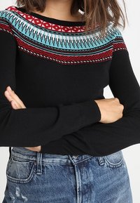 Pull noir avec un motif tricoté coloré sur l'empiècement, comprenant des motifs rouges, turquoise et noirs. Manches longues et silhouette ajustée.