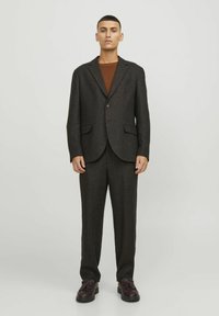 Suit scuro con texture, giacca a un bottone e pantaloni coordinati, caratterizzati da sottili striature rosse e blu, abbinato a scarpe marroni.