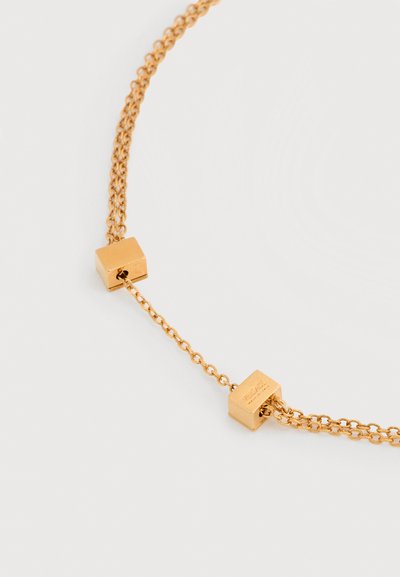 Κολιέ με χρυσή αλυσίδα και δύο μικρές χρυσές χάντρες σε σχήμα κύβου σε λευκό φόντο.