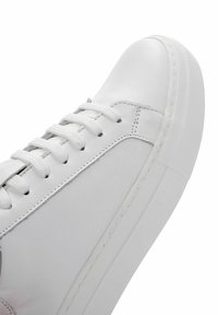 White leather sneaker with a rounded toe, textured outsole, and woven laces. Features contrasting stitching and minimalistic design.