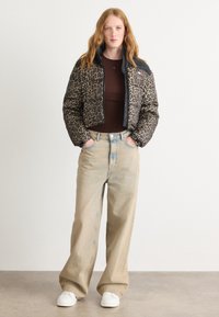 Puff jakke med leopardmønster, svart krage og glidelås. Kombinert med lysebeige vide jeans og hvite joggesko.