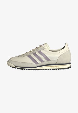 Niski beżowy sneaker Adidas z fioletowymi trzema paskami, zamszowym noskiem i piętą, teksturowaną podeszwą oraz zapięciem na sznurowadła.