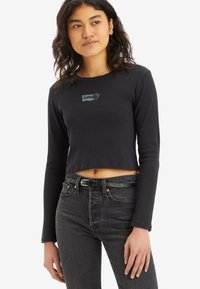 Fekete, hosszú ujjú, crop top Levi's logóval ezüstszínben. Magas derekú fekete farmernadrággal és fekete övvel párosítva. Sima szövettextúra.