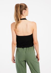 Top corto negro con diseño de cuello halter, combinado con pantalones sueltos de color verde claro. Textura de tela suave, estilo minimalista.