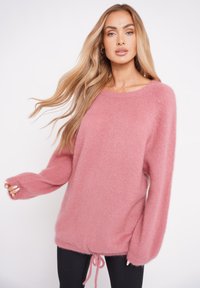 Flauschiger rosa Pullover mit einem runden Ausschnitt, langen Ärmeln mit Fallansatz und einem Kordelzug am Saum für anpassbare Passform. Die weiche Textur ist auffällig.