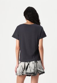T-shirt en coton gris foncé avec des manches courtes retroussées, associé à une jupe en denim noir et blanc à fronces, avec un design évasé.