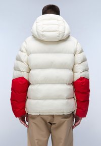 Giacca a vento imbottita con corpo principale bianco, maniche rosse e cappuccio. Presenta sezioni trapuntate e una superficie liscia e lucida.
