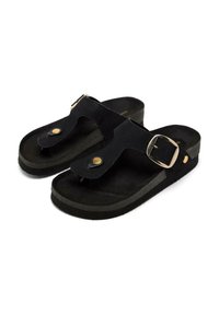 Sandales thong noires avec une tige en suede texturé, un détail en boucle en laiton et une semelle en caoutchouc gris foncé contrastante. Design plat et ouvert.
