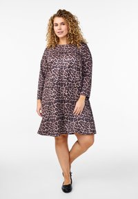 Abito leopardato con maniche lunghe, scollatura rotonda e gonna svasata. Realizzato in tessuto morbido con una leggera lucentezza; le tonalità di colore sono marrone e nero.