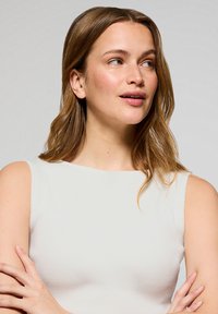 Top sin mangas de rayas blancas con escote redondo. Textura suave y diseño ajustado, combinado con un peinado natural y maquillaje mínimo.