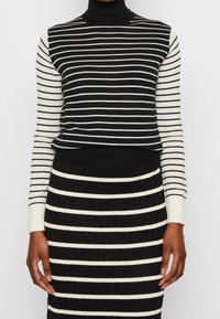 Gestreifter Pullover in Schwarz-Weiß mit hohem Kragen, langärmlig und mit gerippter Textur, kombiniert mit einem passenden gestreiften Rock.
