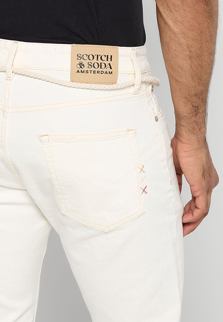 Jeans de mezclilla blanca con un bolsillo trasero con costuras de colores en naranja, amarillo y rojo. Etiqueta de logo de Scotch & Soda en la cinturilla.