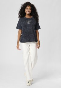 Marineblaues Acid-Wash-T-Shirt mit kurzen Ärmeln und rundem Halsausschnitt, kombiniert mit offwhite Hosen im weit geschnittenen Stil und hellen Sneakers.