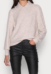 Helles rosa Sweatshirt mit einem Kragen, der mit Perlen verziert ist, strukturiertem Strickstoff, gerippten Bündchen und Saum, kombiniert mit schwarzen, eng anliegenden Lederhosen.