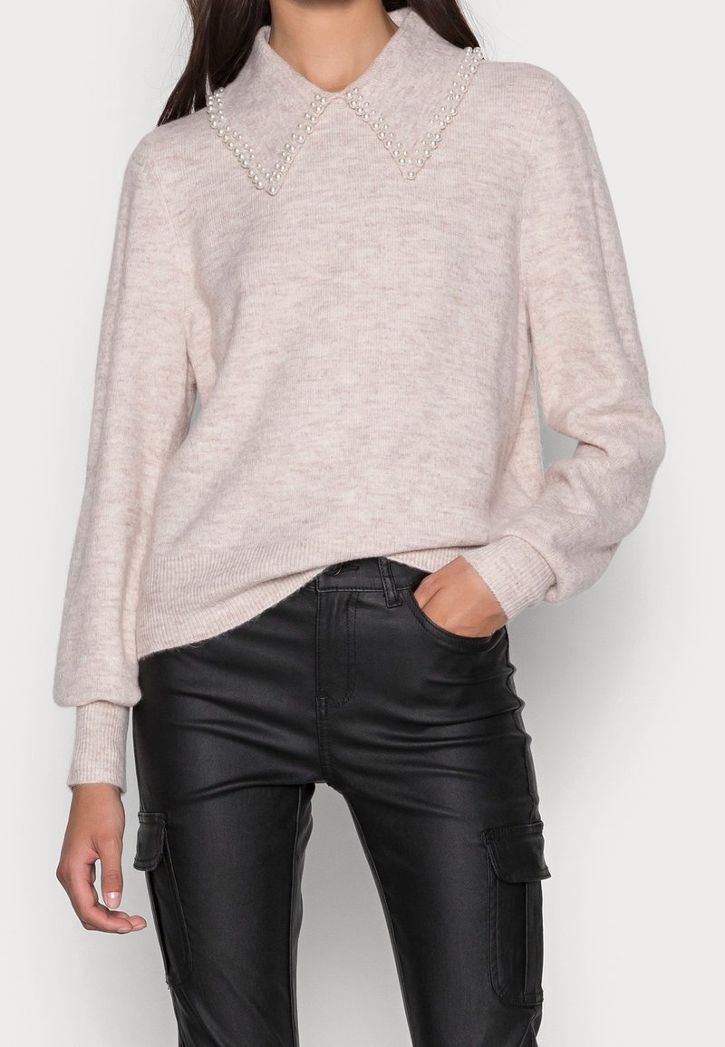 Maglione rosa chiaro con colletto accentato da perle, tessuto a maglia testurizzato, polsini e orlo a coste, abbinato a pantaloni in pelle neri aderenti.