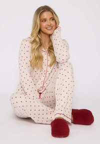 Witte pyjama set met kleine rode hartjespatronen, rode contrasterende bies en een losse fit; gecombineerd met schattige rode sloffen.