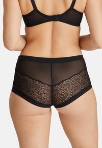 Braguitas negras con borde de encaje y un panel trasero transparente con bordado floral. Cinturilla elástica suave, ajuste de altura media y detalles intrincados.