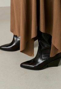 Mustad nahast platvormi ankle saapad terava ninaga, osaliselt kaetud voolava pruunist kangast, mis näitab sujuvat tekstuuri ja elegantset disaini.