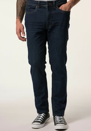 Dark blue denim jeans with a slim fit, five pockets, light stitching, and a classic button and zipper closure, paired with black sneakers.
