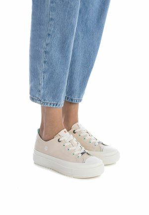 Zapatillas de lona beige con un acabado texturizado, suela de goma blanca, detalles en verde y naranja, y cierre de cordones.