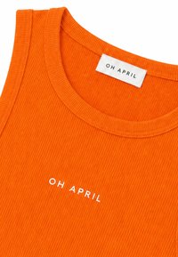 Gros plan d'un débardeur en tissu côtelé orange vif avec un col rond et le texte blanc « OH APRIL » sur la poitrine ainsi qu'une étiquette à l'intérieur du col.