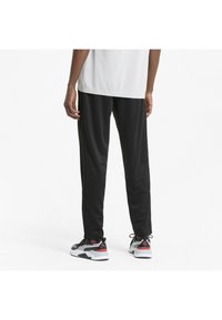 Sorte atletiske bukser med en glat overflade, der har en tapered pasform og elastisk talje. Sammen med sorte og røde sneakers.