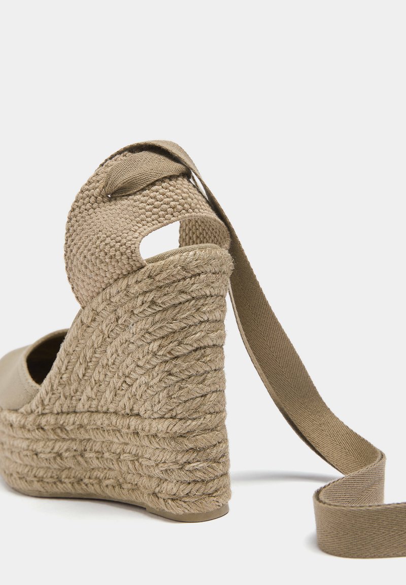 Beige Espadrille-Plateauschuhe mit geflochtenem Juteabsatz, offenem Design auf der Rückseite und Stoffknöchelriemen. Glatte Textur und runde Zehenform.