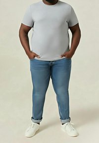 Šedé tričko s krátkým rukávem, modré úzké džíny, bílé boty na nazutí. Tričko má hladkou texturu; džíny mají mírně vybledlý vzhled.