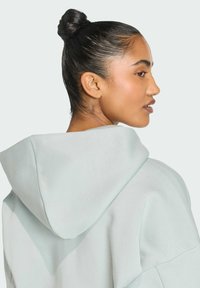 Svetlomodrá mikina s kapucňou a uvoľneným strihom, ktorá má jemnú textúru a zaoblené ramená. Viditeľná kapucňa a detaily šitia.