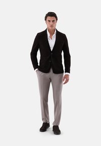 Braunes Cord-Blazer mit zwei Knöpfen, kombiniert mit hellgrauer Hose und dunklen Schuhen. Weißes Hemd darunter sorgt für Kontrast.