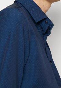 Marinblå knappad skjorta i mjukt texturerad tyg med ett subtilt prickmönster och klassisk krage, med en knäppt placket.