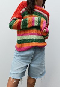 Meerlagige gebreide trui met horizontale strepen in rood, groen, oranje, roze en crème. Gecombineerd met lichtblauwe distressed denim shorts.