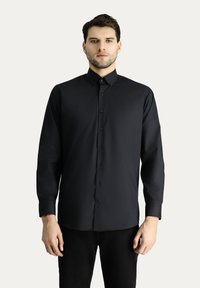 Camisa negra de manga larga con cierre de botones en el frente, un collar clásico y una textura suave. Corte recto con puños abotonados y un brillo sutil.