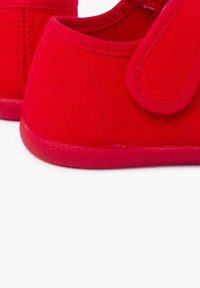 Rote Leinen-Schuhe mit einem Klettverschluss, abgerundeter Zehenpartie, strukturiertem Stoff und einer glatten Gummisohle. Einfaches Design ohne zusätzliche Verzierungen.