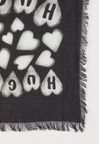 Czarny szalik z białymi wzorami serc oraz napisem "HUG" w pogrubionych czarnych literach, z frędzlami na brzegach dla tekstury.