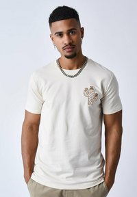 Beige t-shirt met korte mouwen, voorzien van een geborduurd cactusontwerp op de borst. Heeft een ronde hals en een gladde, zachte textuur.