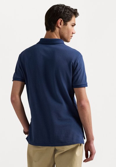 Navyblauwe katoenen polo met kraag, korte mouwen, een gestructureerde afwerking en een zijvent, gecombineerd met beige broek.