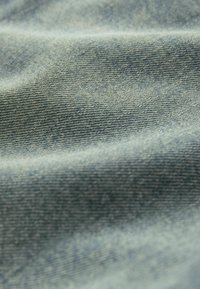 Tissu en denim bleu clair avec une texture lisse et un motif de tissage subtil, montrant des plis et des rides dans le matériau.