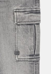 Gray denim cargo pants featuring a patch pocket with a flap, visible stitching, and a logo tag near the pocket. Smooth texture.
